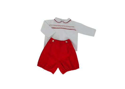 Hand-smocked white long-sleeve baby boy top with red-trimmed collar and matching red knickers, flat lay on white background