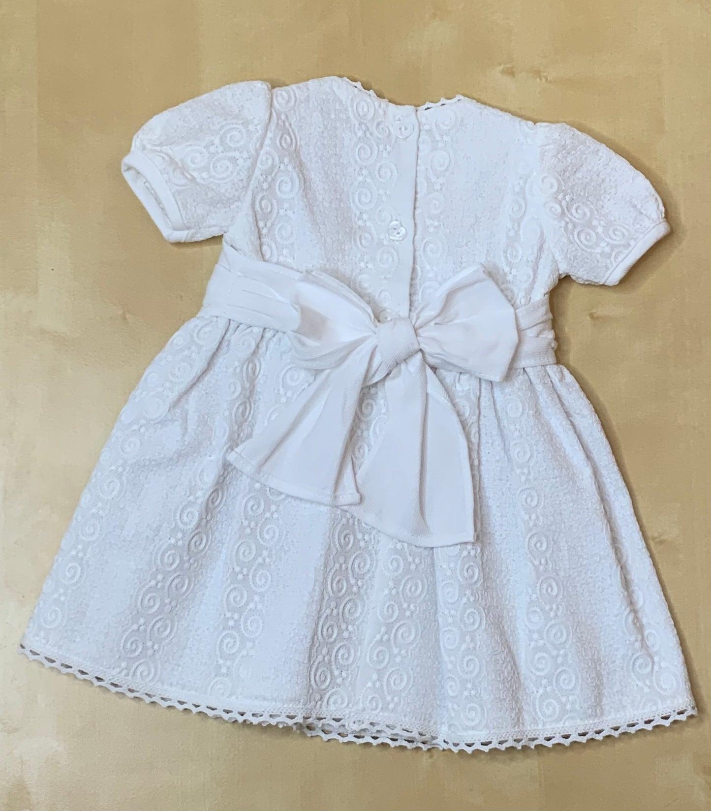 Close-up detail of The Petite Lumière white embroidered cotton fabric and lace trim, button closure, large bow, Alfa Baby Boutique